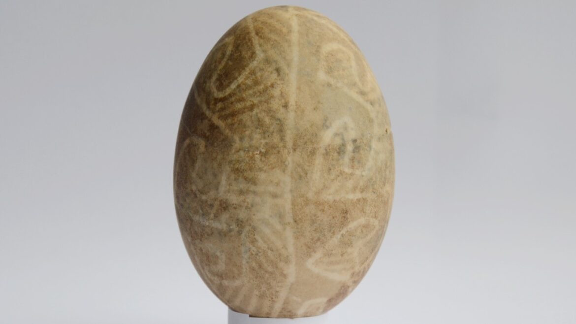 A duck egg decorated with a wax-resist technique that involves light-colored wavy lines against a light-brown-colored eggshell