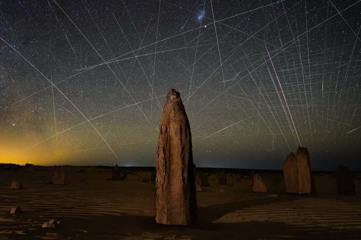light streaks in the night sky above an arid landscape with rocky forms